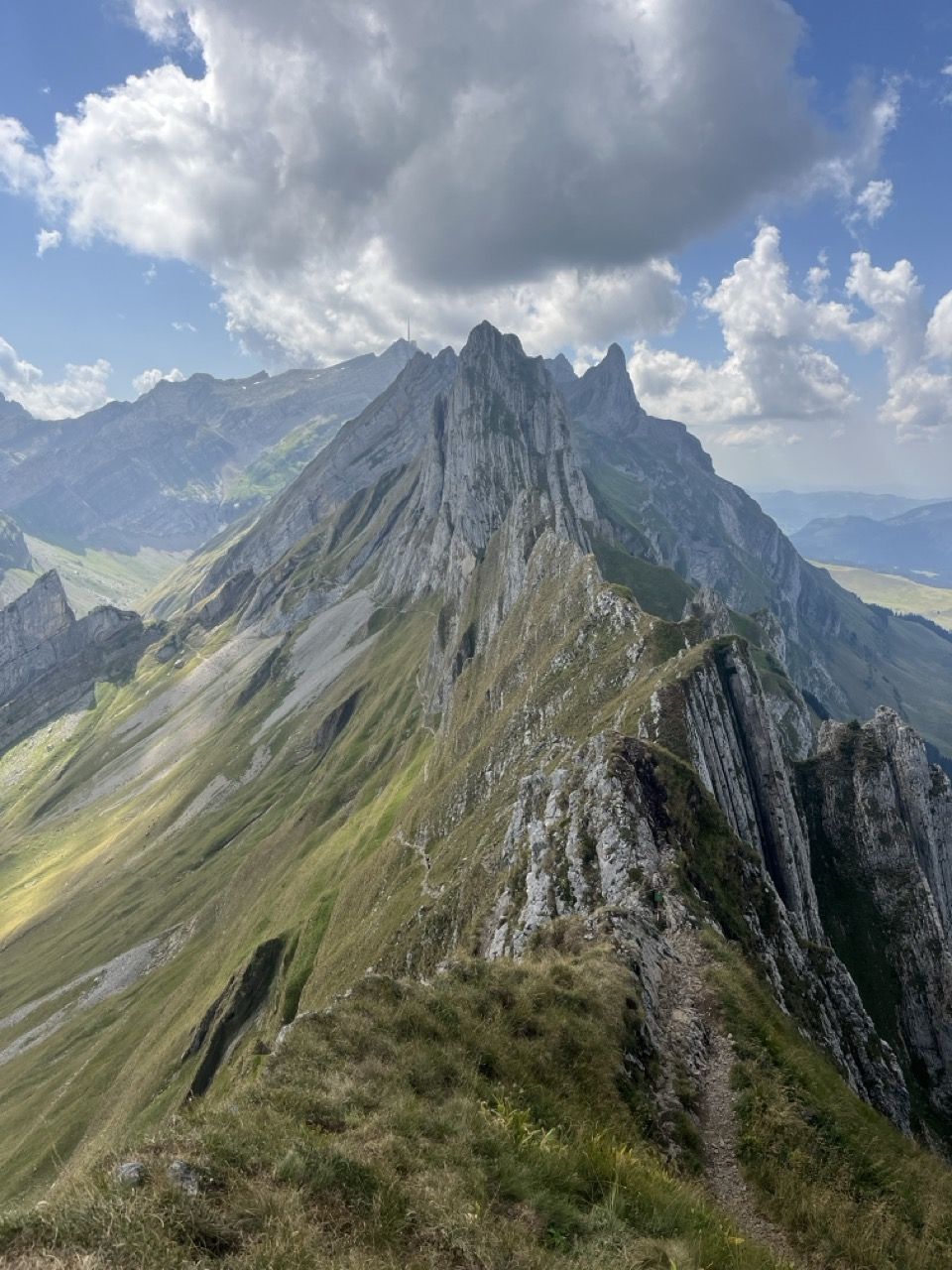 Wanderweg auf einem Grat, dahinter eine felsige Bergkette